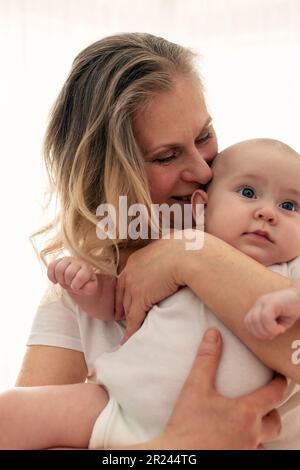 A loving grandmother gently hugs and kisses her granddaughter. Grandmother looks at her granddaughter. Family happiness. White background Stock Photo