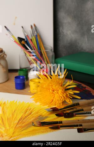 Canvas with colorful painting, yellow chrysanthemum and brushes on table Stock Photo