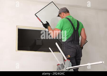 Worker on folding ladder installing window indoors Stock Photo