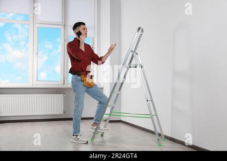 Handyman talking on phone while climbing up stepladder in room Stock Photo