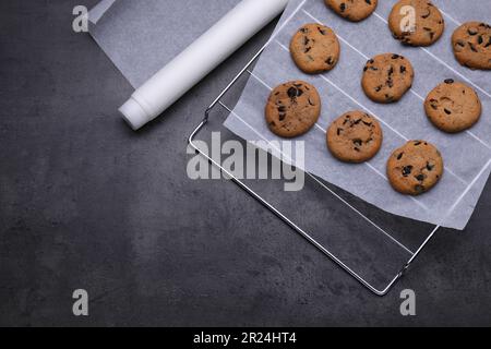 Roll of parchment baking paper and cooling rack with tasty cookies on dark grey table, flat lay. Space for text Stock Photo
