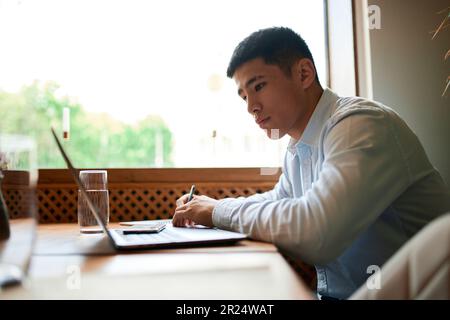 Male freelancer in suit working on new startup project making internet researchers, analyzing data using laptop in city cafe. Concept of freelance Stock Photo