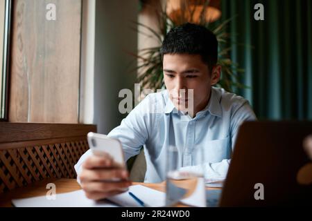 Confident busy male freelancer, businessman doing remote job using smartphone searching information for presentation in cafe Stock Photo