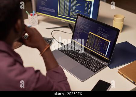 Rear view of African American developer typing computer codes on laptop sitting at his workplace Stock Photo