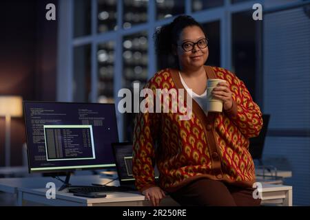 Portrait of African American programmer looking at camera while working till late night in office with cup of coffee Stock Photo