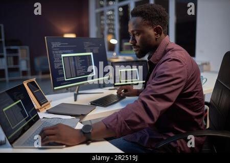 African American programmer concentrating on his online work on computers while working in office till late evening Stock Photo