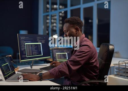 African American developer developing software on computer using codes while working in office till late night Stock Photo