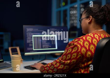 Rear view of female programmer working with computer codes at her workplace till late night in office Stock Photo