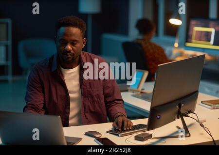 African American developer working on computer at his workplace in dark IT office Stock Photo