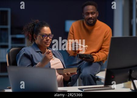 Programmers having lunch while discussing computer program on computer in dark office Stock Photo