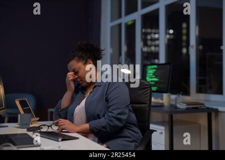 Exhausted woman sitting at her workplace with computer, she working till late night in office Stock Photo