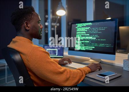 African American developer sitting at his workplace and concentrating on writing computer codes during his late work in office Stock Photo