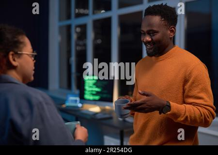 Colleagues drinking coffee and talking to each other while working in office till late night Stock Photo