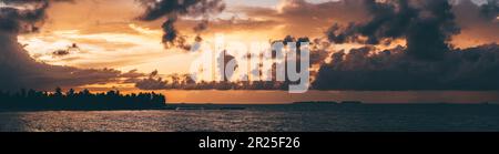 A stunning panoramic view of the sea during a breathtaking Maldivian sunset with orange sun behind dark-colored clouds and a silhouette of the trees i Stock Photo