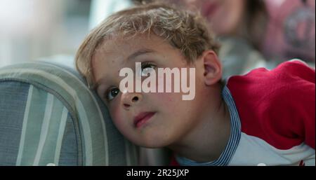 Toddler child staring at TV screen hypnotized. Boy watching screen on sofa before bed Stock Photo