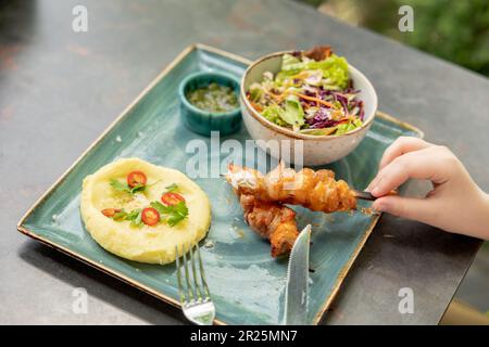 Mashed potatoes, chicken kebab, salad. Children's menu in the restaurant. Child's hand holding a barbecue Stock Photo
