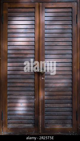 Wooden door with ventilation from lamellas, sun protection blinds door closed with a padlock, close-up, vertical frame. Stock Photo