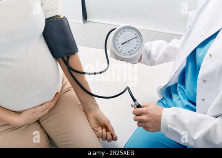 doctor measuring blood pressure of pregnant woman on maternity leave while visit by perinatal center. Examinations during pregnancy Stock Photo