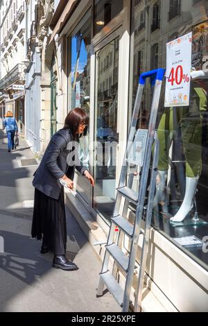 Elegantly dressed woman cleaning shop window - Tours, Indre-et-Loire (37), France. Stock Photo