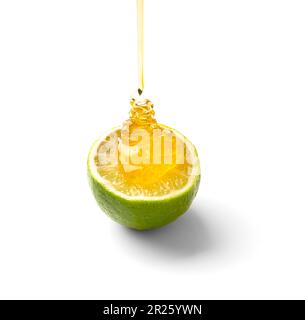Honey pours on a cut juicy lime on a white background close-up. Half lime and pouring honey on isolation. Stock Photo