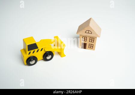 Yellow toy bulldozer and a house. Encroachment on private property. Illegal buildings and construction. Violation of building codes. Demolition proces Stock Photo