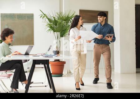 Multiethnic Businesswoman And Businessman Using Tablet Reading Papers In Office Stock Photo