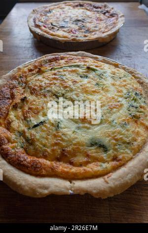 Quiche. Fresh eggs mixed with vegetables, bacon, ham, sausage, cheese, and Broccoli. The round shape on rustic wooden board. Stock Photo