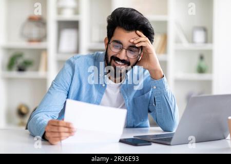 Young Indian Male Self-Entrepreneur Working With Papers At Desk In Home Office Stock Photo