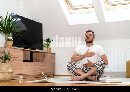 Man doing breathing exercise sitting on floor at home in half lotus position. Stock Photo