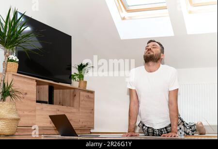 Young adult man doing stretching yoga exercise on yoga mat at home. Stock Photo