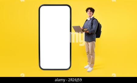 Student Using Laptop Posing With Huge Phone On Yellow Background Stock Photo