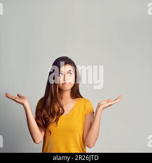 I just cant make up my mind...Studio shot of an attractive young woman showing copyspace against a grey background. Stock Photo