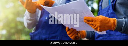 New project. Close up shot of two builders standing outdoors with an open blueprint discussing the cottage construction Stock Photo