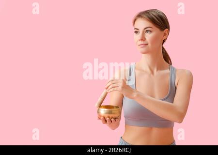 Young woman with Tibetan singing bowl on pink background Stock Photo