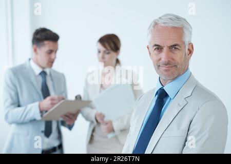 He has a good business team. Portrait of an older business man with business people in the background. Stock Photo
