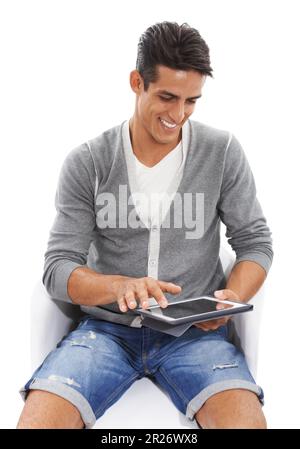 Enjoying modern technology. A handsome smiling young man sitting and smiling while using a ipad against a white background. Stock Photo