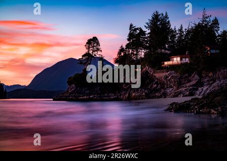 Sunset over a small bay where the purple color invades the ocean water and the red of the clouds against a background of blue sky, are inserted behind Stock Photo