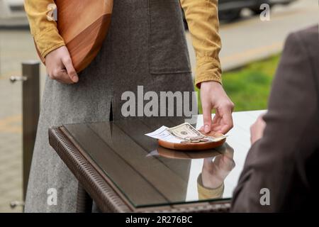 Waitress taking tips from wooden table in outdoor cafe, closeup Stock Photo