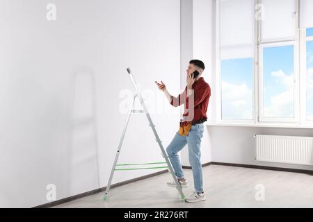 Handyman talking on phone while climbing up stepladder in room Stock Photo