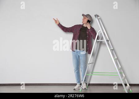 Handyman talking on phone near stepladder in room Stock Photo