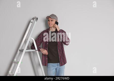 Handyman leaning on stepladder while talking on phone near white wall Stock Photo