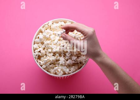 Woman taking delicious popcorn from paper bucket on pink background, top view Stock Photo