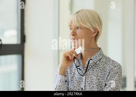 Woman with short hair looks out window holding glasses Stock Photo