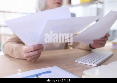 Serious grey haired woman studies reports sitting at table Stock Photo
