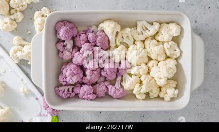 Cauliflower florets, white and purple, close-up in baking pan, flat lay, light grey stone background. Stock Photo
