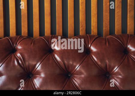Close-up of a piece of artificial brown leather on a wooden background, upholstered furniture in retro Chesterfield style with a deep diamond pattern and buttons. High quality photo Stock Photo