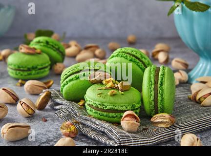Green colored pistachio macarons with pistachios and mint on gray wooden background. Close up Stock Photo