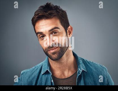 Unshaven but still as smooth as ever. Studio portrait of a handsome young man posing against a grey background. Stock Photo