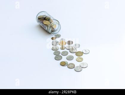 Coins spread out from a glass jar on isolated white background Stock Photo