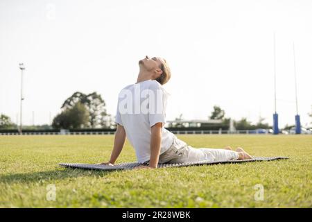surface level of young yoga man practicing cobra pose with closed eyes on green grass outdoors Stock Photo